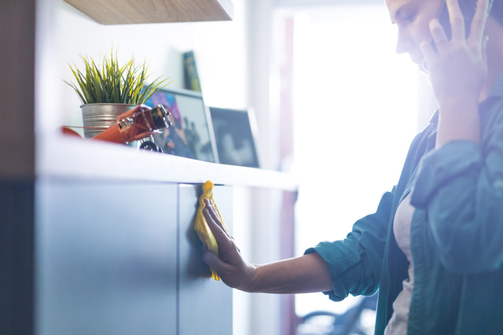 Woman polishing furniture in the living room and talking on mobile phone